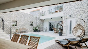 Ein moderner Außenbereich mit Pool, Holzmöbeln, Steinwänden und einer Treppe zu einer erhöhten Ebene.
