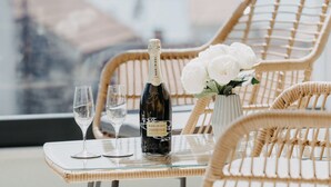 Ein Balkon mit Korbstühlen, einem Glastisch, zwei Weingläsern, einer Champagnerflasche und einer Vase mit weißen Blumen.