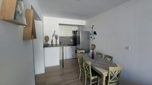 Eine moderne Küche mit weißen Schränken, ein Essbereich mit Holztisch und Stühlen sowie eine kleine Kücheninsel mit Spüle.