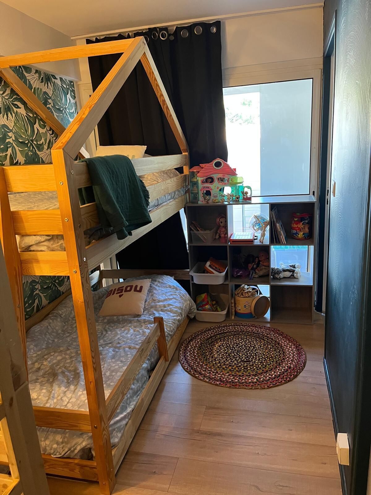 Une chambre avec un lit superposé, une bibliothèque et un petit tapis.