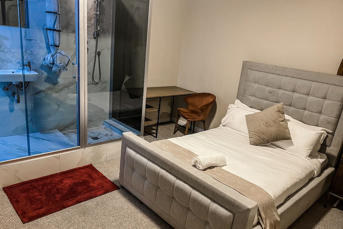 Quarto com cama, escrivaninha, cadeira e área de chuveiro.