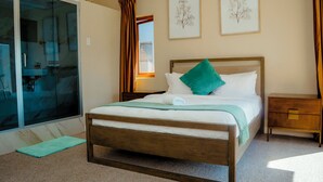 A bedroom with a wooden bed, a green pillow, a nightstand, and two framed botanical prints on the wall.