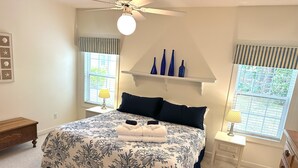 Un dormitorio con cama, dos mesitas de noche, ventilador de techo y ventana con persianas.