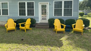 Una casa con un porche delantero, tres sillas amarillas tipo Adirondack y una mesita azul.