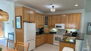 Una cocina con armarios de madera, un refrigerador blanco, un microondas, un horno y una mesa de comedor con sillas.