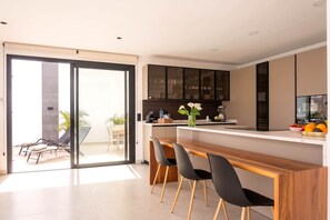 A modern kitchen with a dining area, sliding glass doors leading to an outdoor seating area, and a built-in cabinet with glass doors.