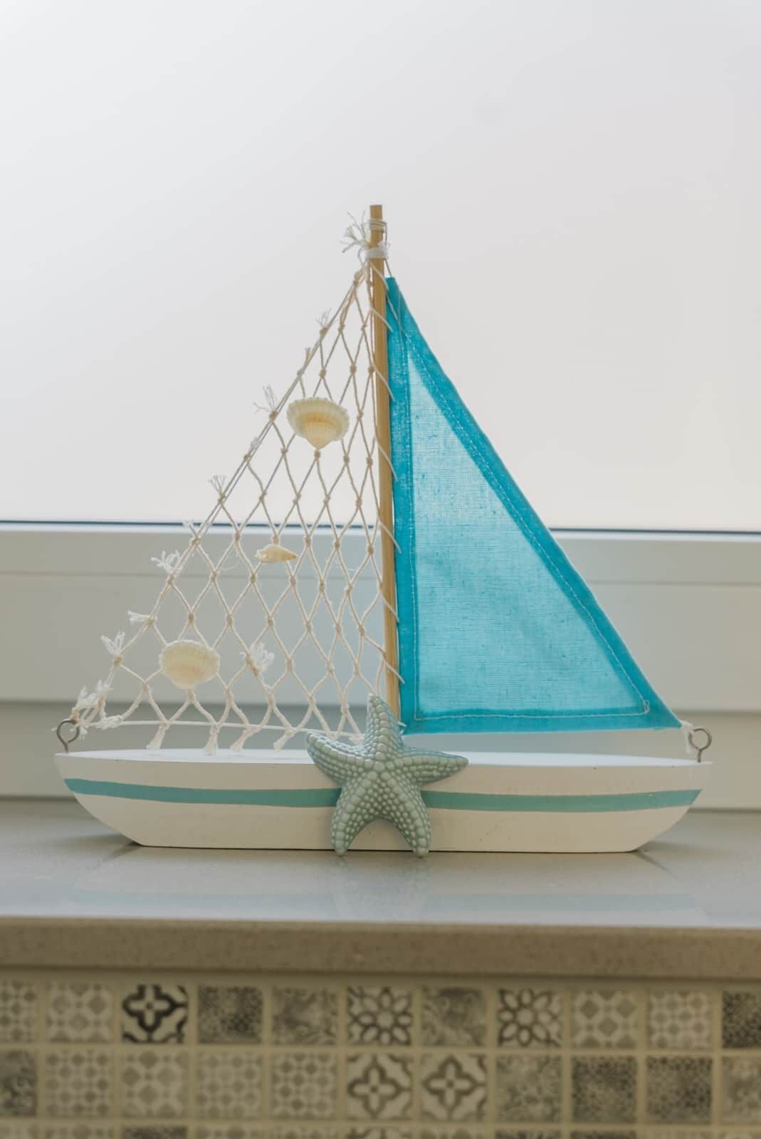 A decorative sailboat model with a starfish decoration on a shelf.