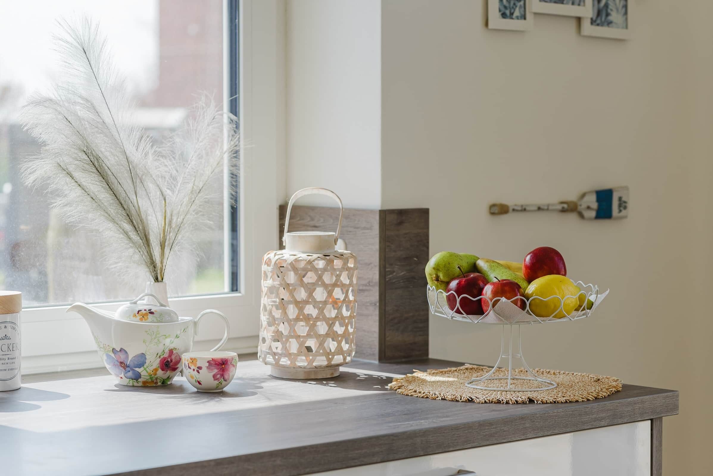 Eine Küchenarbeitsplatte mit Teekanne, Tasse, dekorativer Vase und Obstschale.