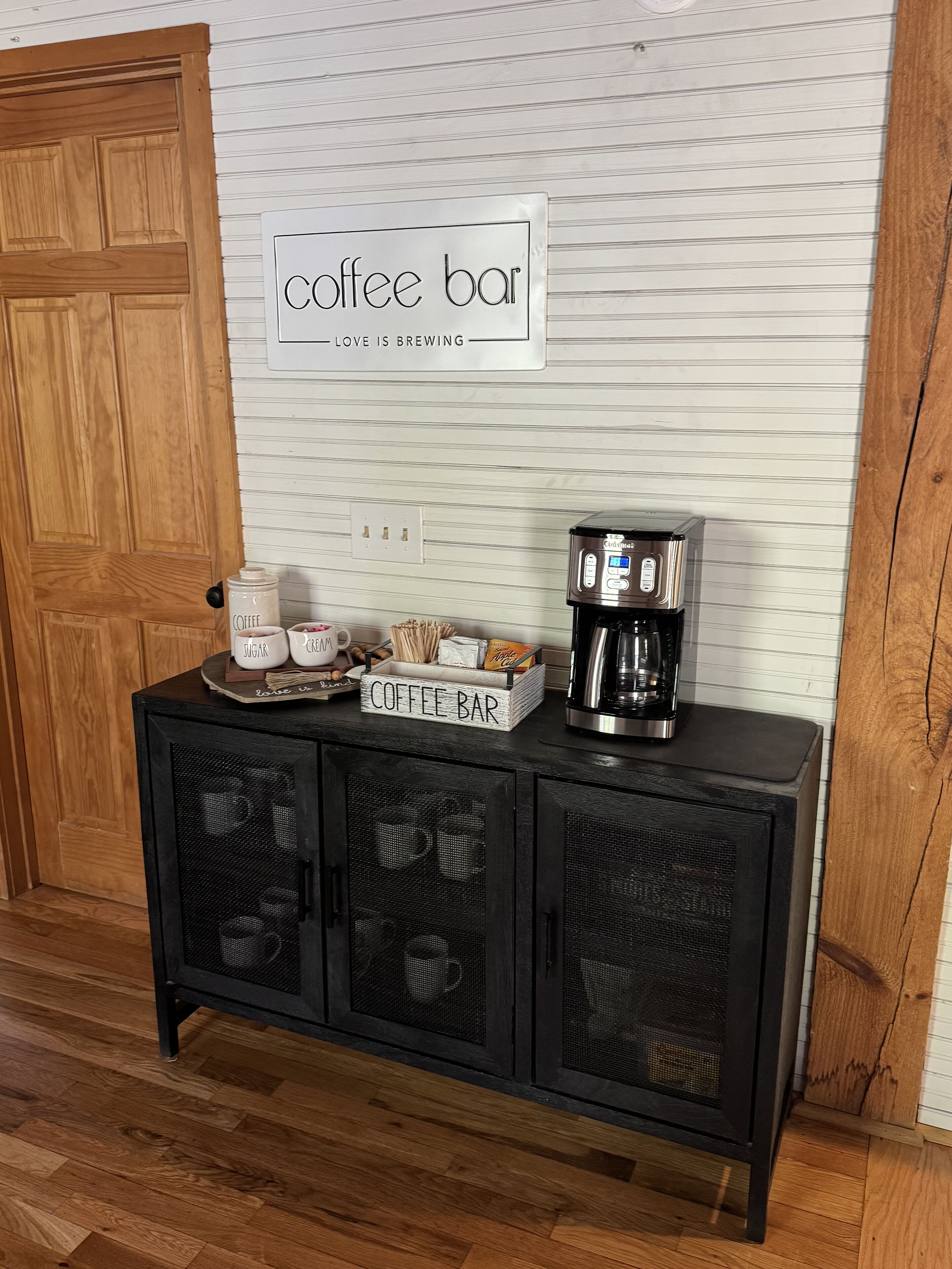 A coffee bar setup with a coffee machine, sugar, cream, and a sign that reads "coffee bar love is brewing".