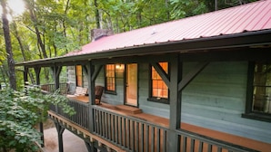 A wooden cabin with a porch, surrounded by trees.