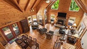 A spacious wooden cabin with a dining area, living room, fireplace, and a staircase leading to an upper level. - Secluded Creekside Cabin - Fire Pit, Deck & Mountain Views, Sleeps 8 (Lake Lure)