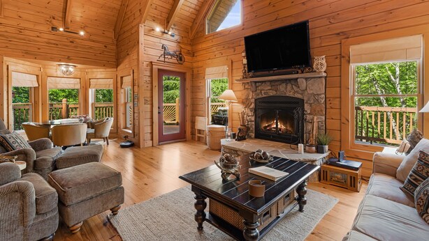 A cozy cabin interior with a stone fireplace, wooden furniture, and a television mounted on the wall. - Secluded Creekside Cabin - Fire Pit, Deck & Mountain Views, Sleeps 8 (Lake Lure)