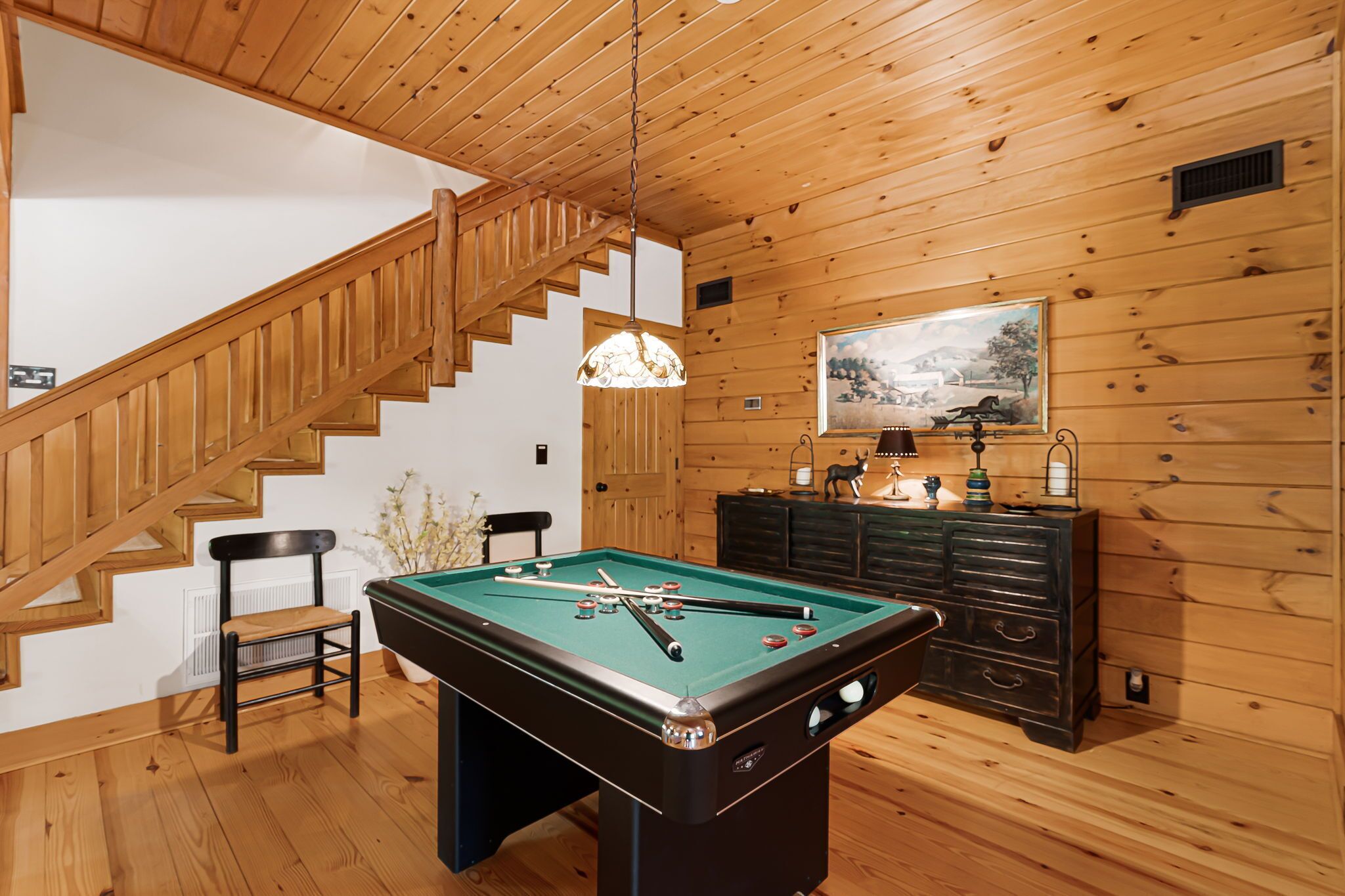 Una habitación con paneles de madera, una mesa de billar, una escalera y un cuadro en la pared.
