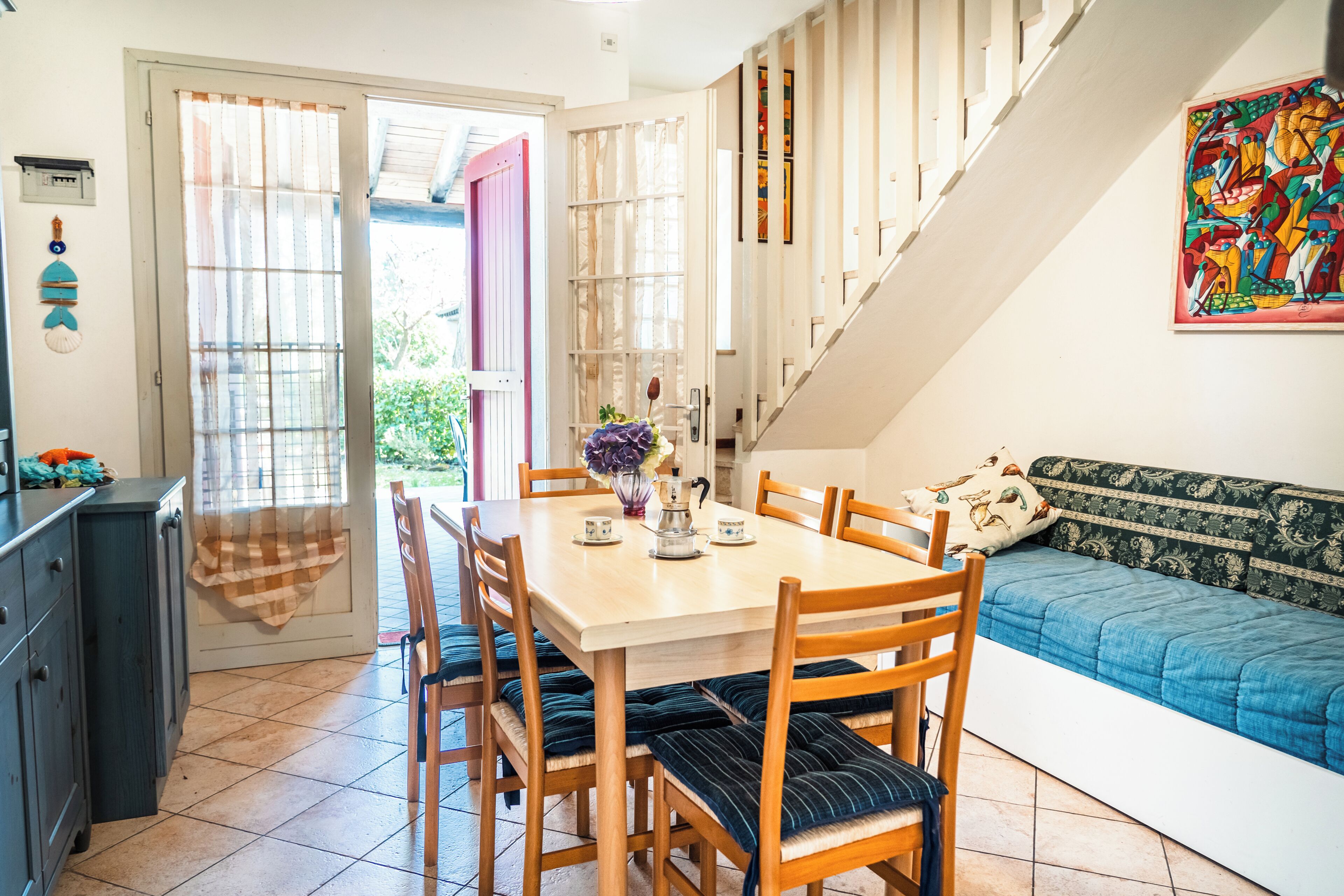 A dining area with a wooden table and chairs, a sofa, and a staircase.