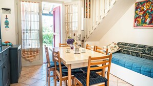 A dining area with a wooden table and chairs, a sofa, and a staircase. - Charming Apartment With Garden and Pool (San Michele al Tagliamento)