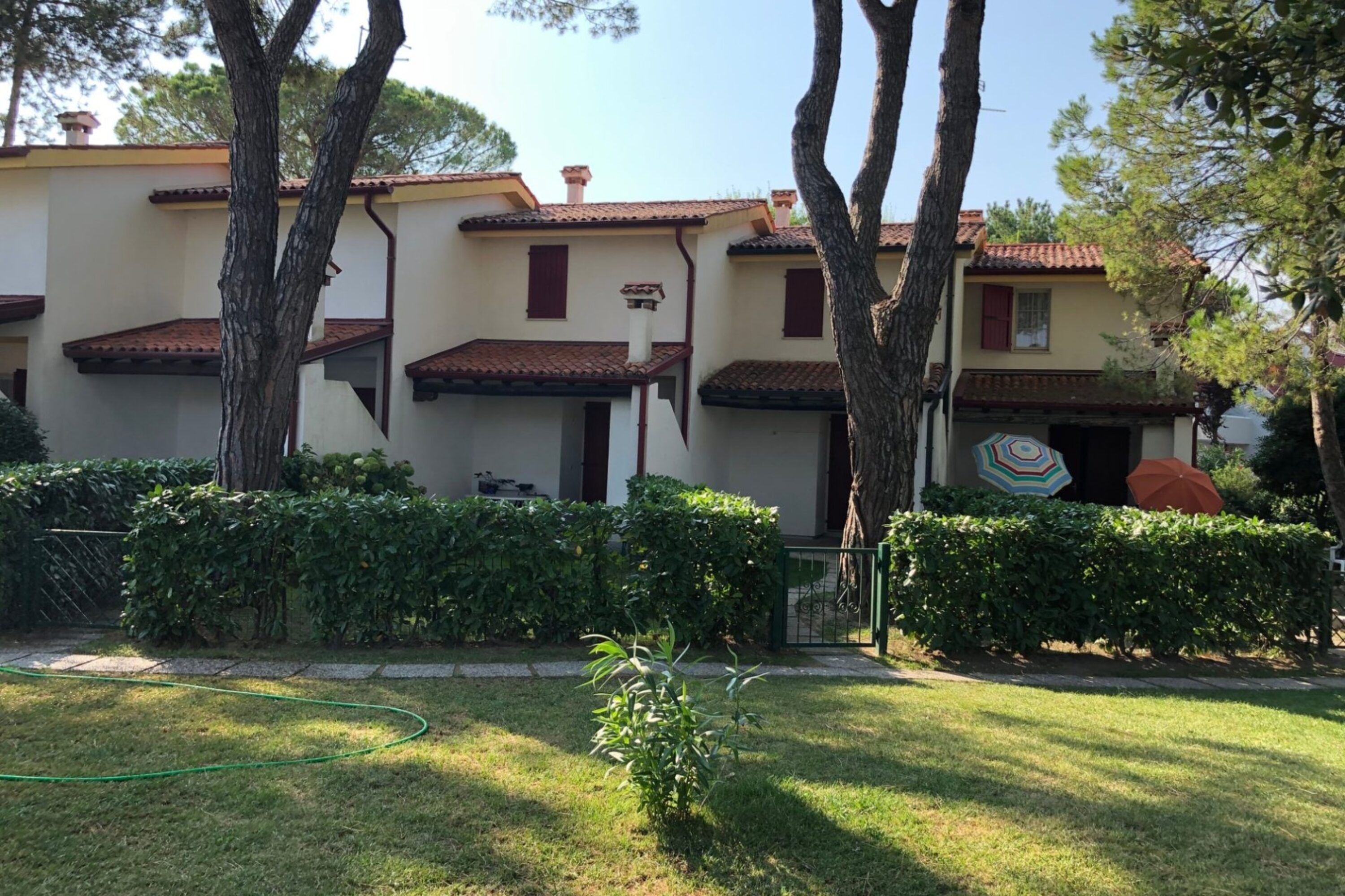 A building with multiple units, each with a tiled roof and a small balcony. There are trees and a well-maintained lawn in front.