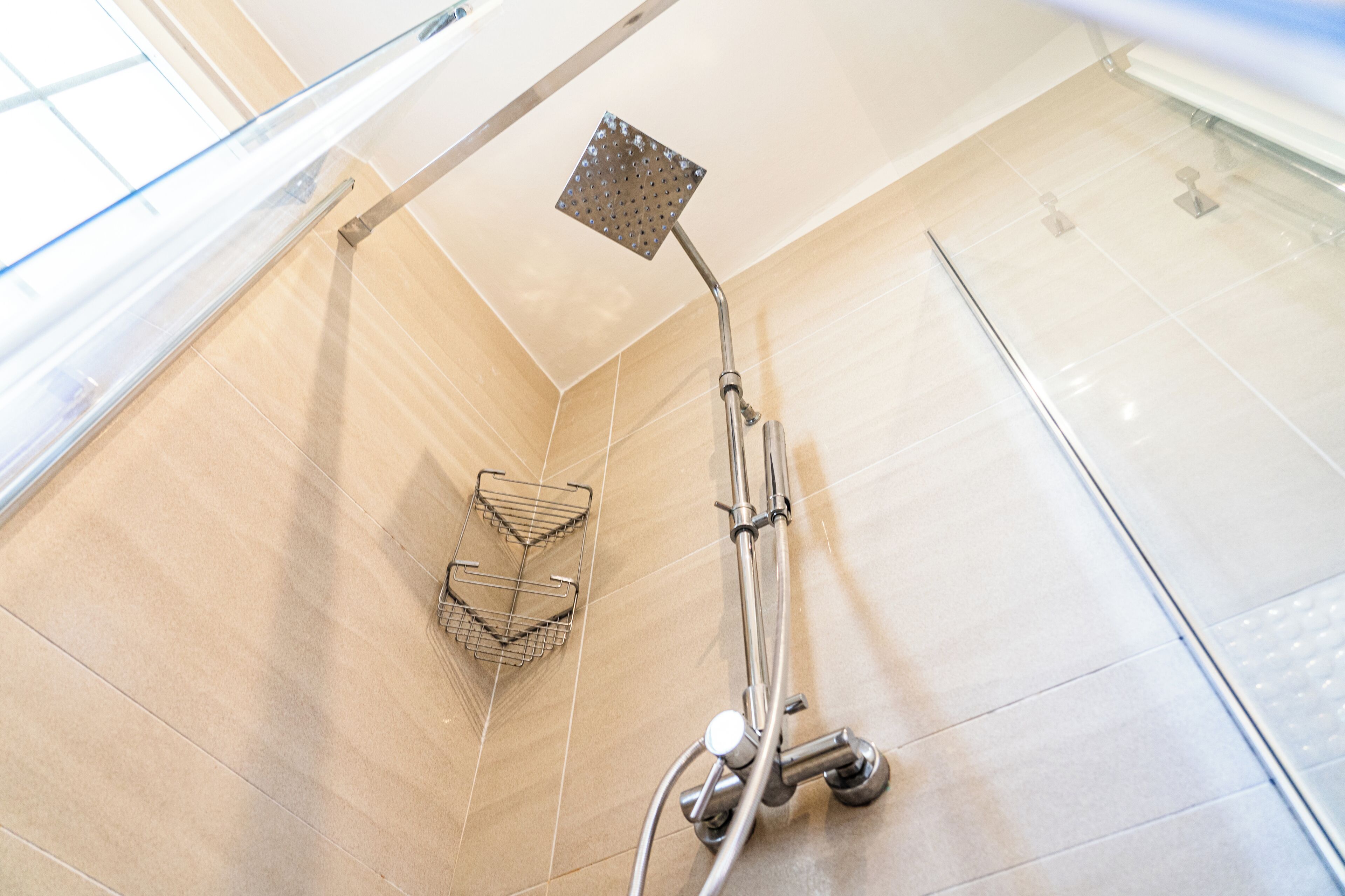 A modern shower with a square head, a handheld showerhead, and a metal shelf.