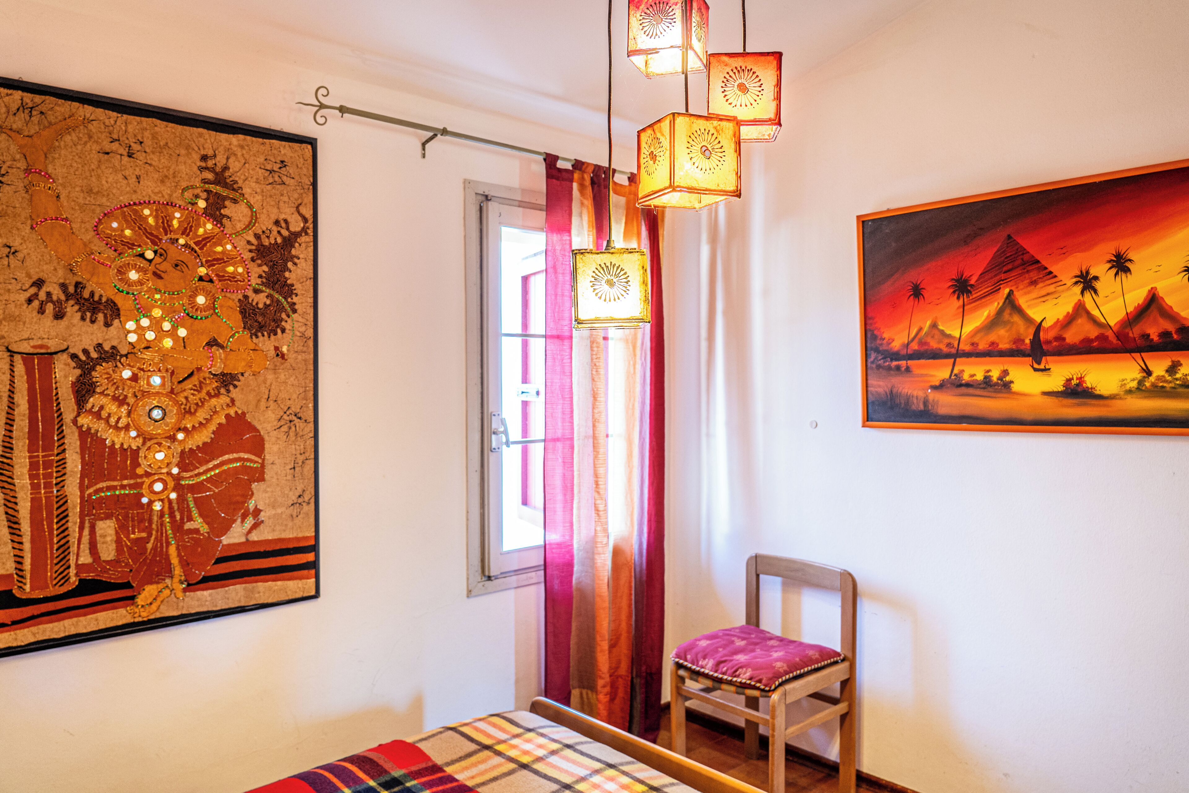 A room with a bed, a chair, a large painting, and a window with curtains.