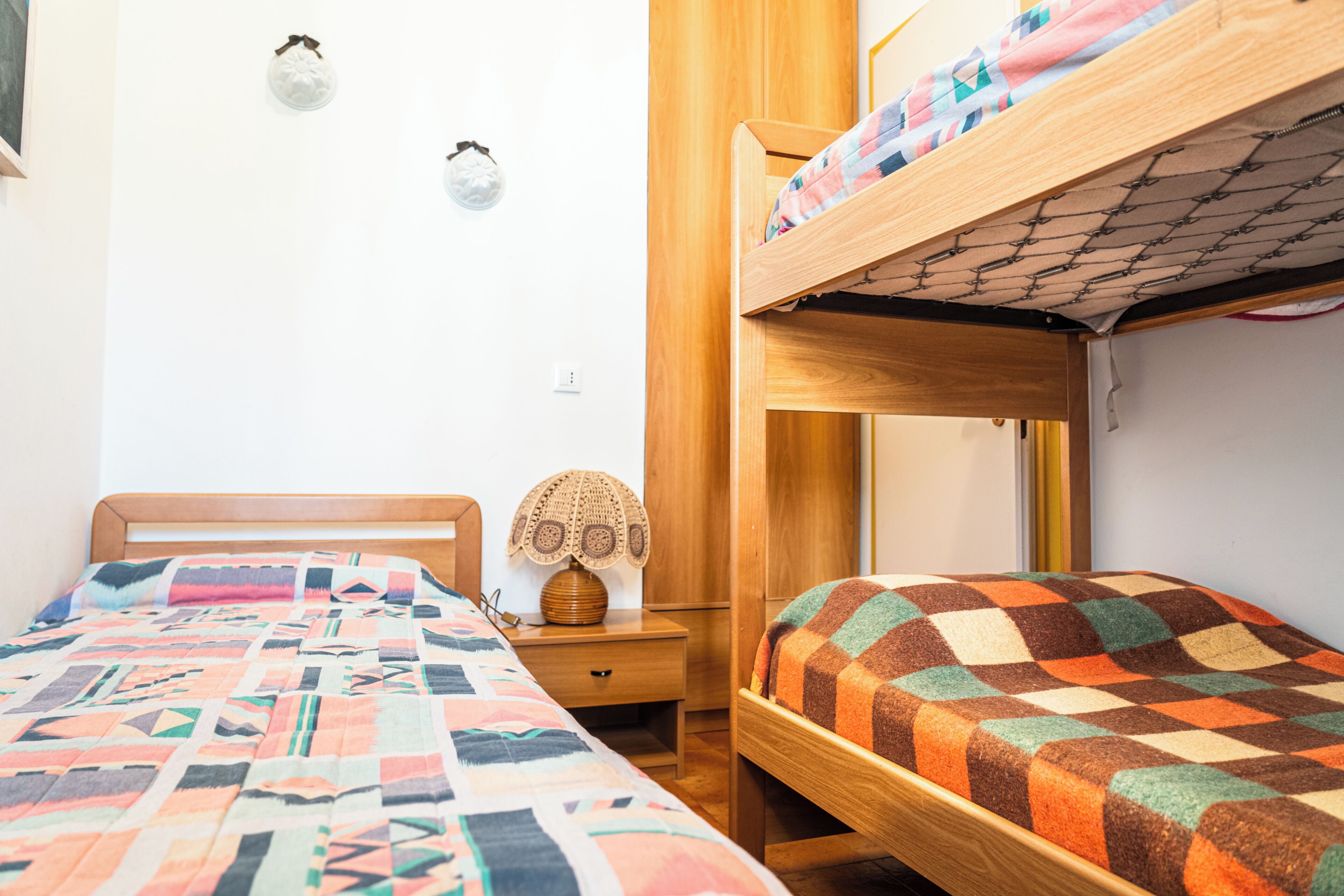 Una habitación tipo dormitorio con dos camas individuales, una mesita de noche de madera, una lámpara y un aplique de pared.