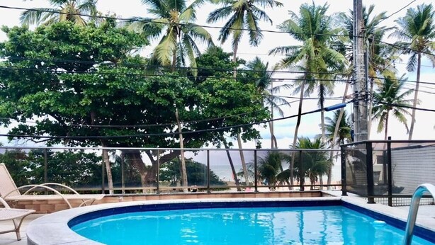 A swimming pool with a curved edge, surrounded by lounge chairs and a view of palm trees and the ocean.