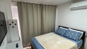 A bedroom with a bed, a TV, a curtain, and an air conditioner.
