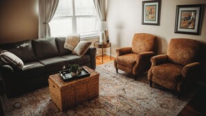 A living room with a dark brown sofa, two patterned armchairs, a woven coffee table, and a patterned rug.
