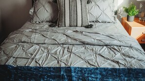 A neatly made bed with a grey headboard, a striped pillow, and a blue throw blanket.