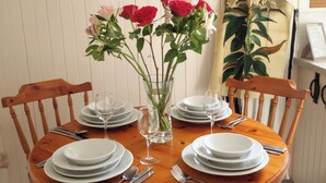 Una mesa de comedor de madera dispuesta con platos blancos, cubiertos y copas de vino, junto con un jarrón de flores rojas y rosas.