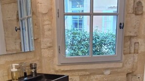 Un bagno con parete in pietra, una finestra, un lavandino con articoli da toilette, un armadietto in legno e un asciugamano bianco su un letto soffice.