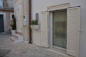 Steps lead up to a stone building with a white door and a sliding glass door with shutters.