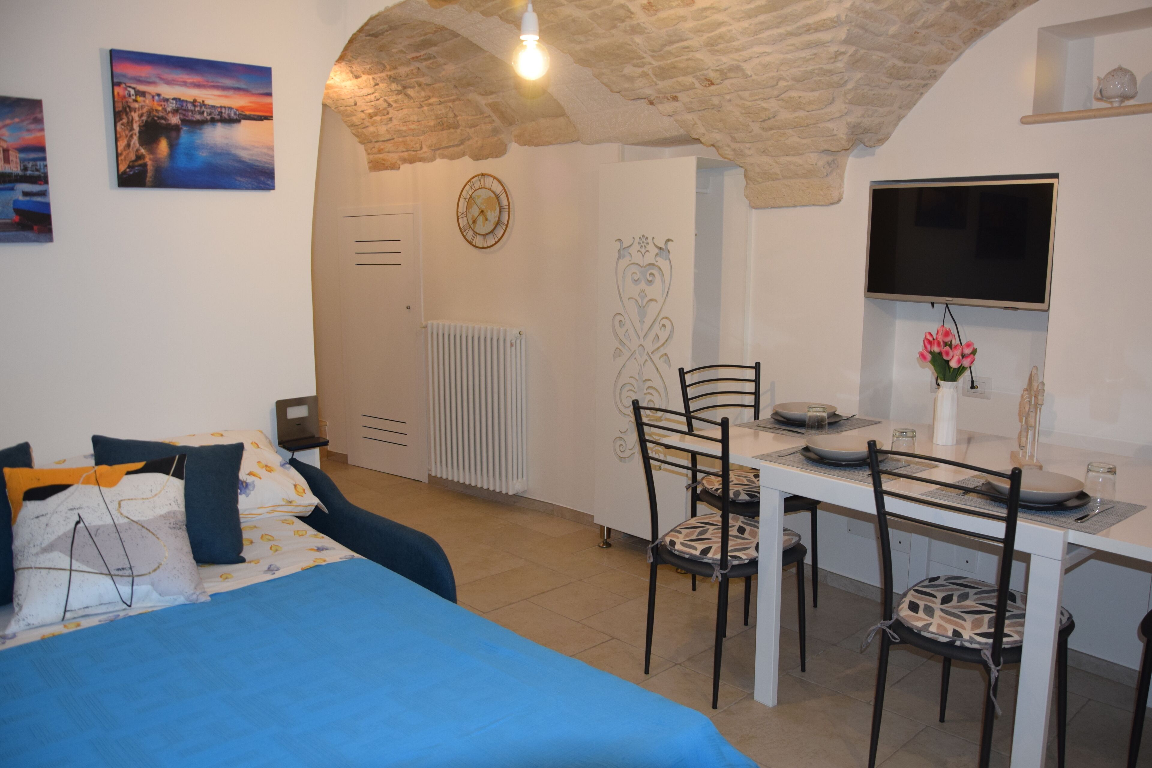 A room with a bed, a dining table with chairs, a TV, and a radiator.