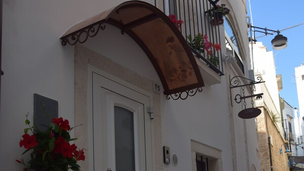 Una estrecha calle adoquinada con un edificio blanco que tiene una puerta, un ventanal pequeño y un balcón con macetas.