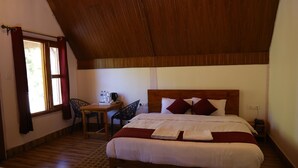 A bedroom with a wooden ceiling, a large bed with white bedding, a desk with a chair, and a window with curtains. - BLESSINGS RESORT (Rajgarhi)