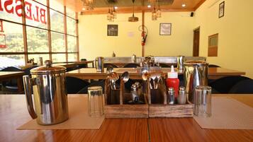 A restaurant with wooden tables, metal serving utensils, and a large window with a view of trees.