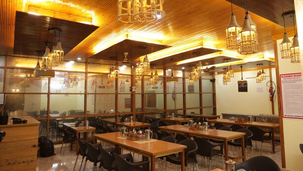 A restaurant with wooden tables and chairs, hanging light fixtures, and large windows. - BLESSINGS RESORT (Rajgarhi)