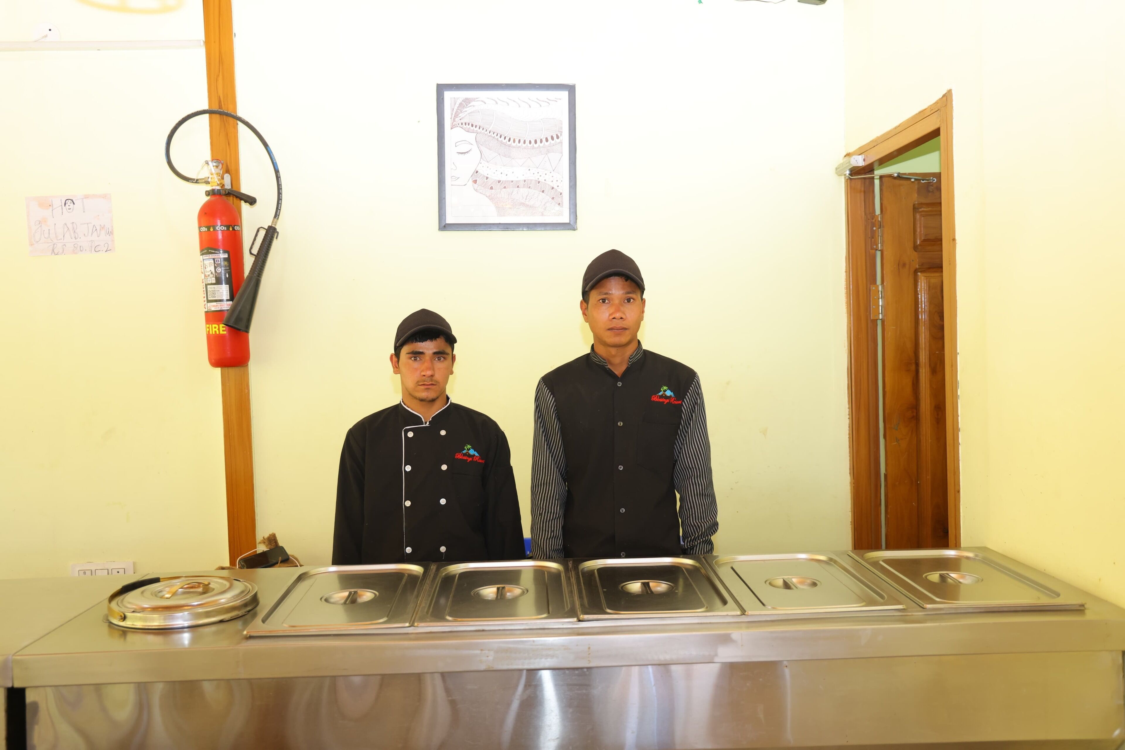 Two individuals in chef uniforms standing in front of a stainless steel buffet with multiple serving stations.