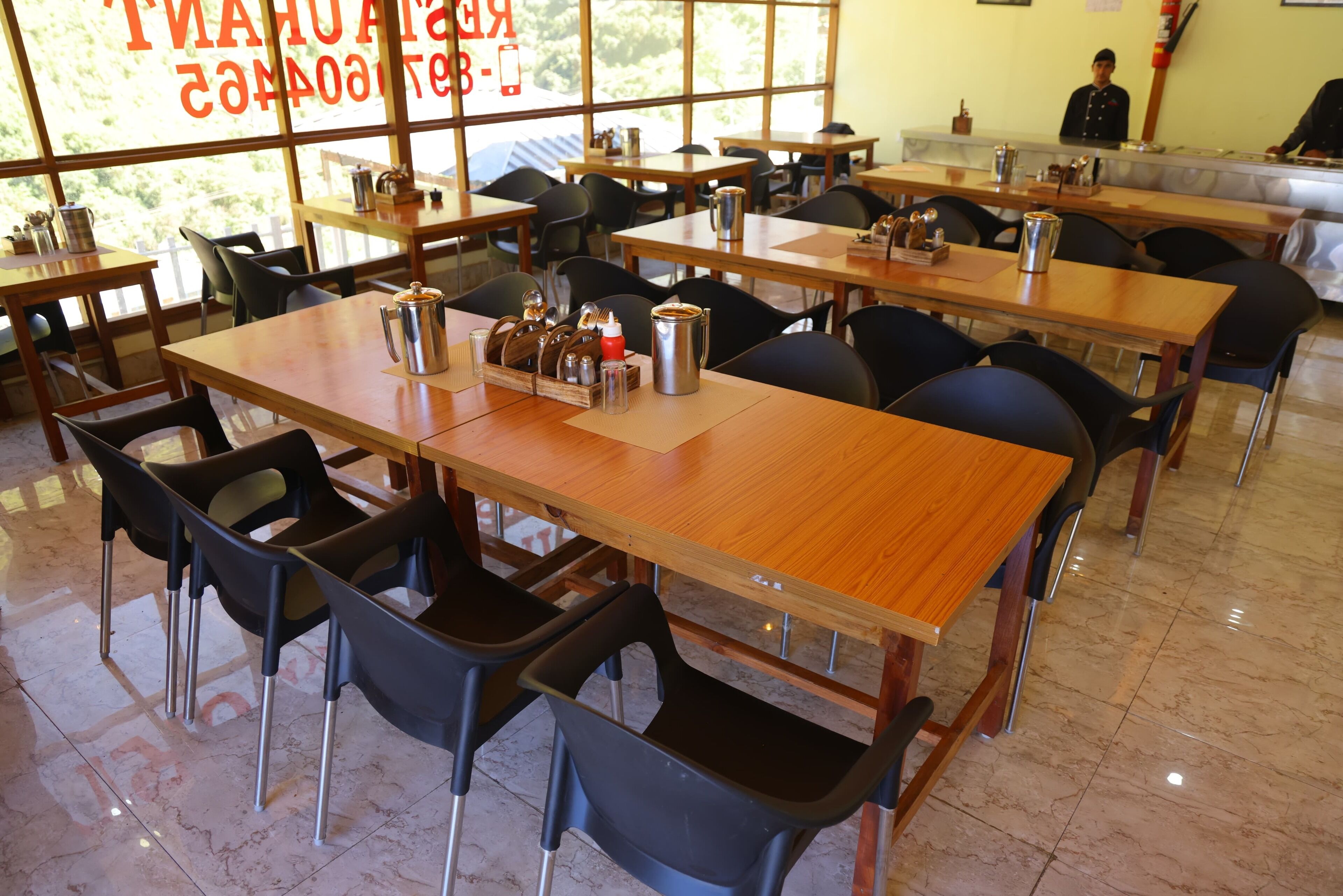 Een restaurant met meerdere houten tafels en zwarte stoelen, waarvan sommige voorzien zijn van kruiden en koffiepotten.