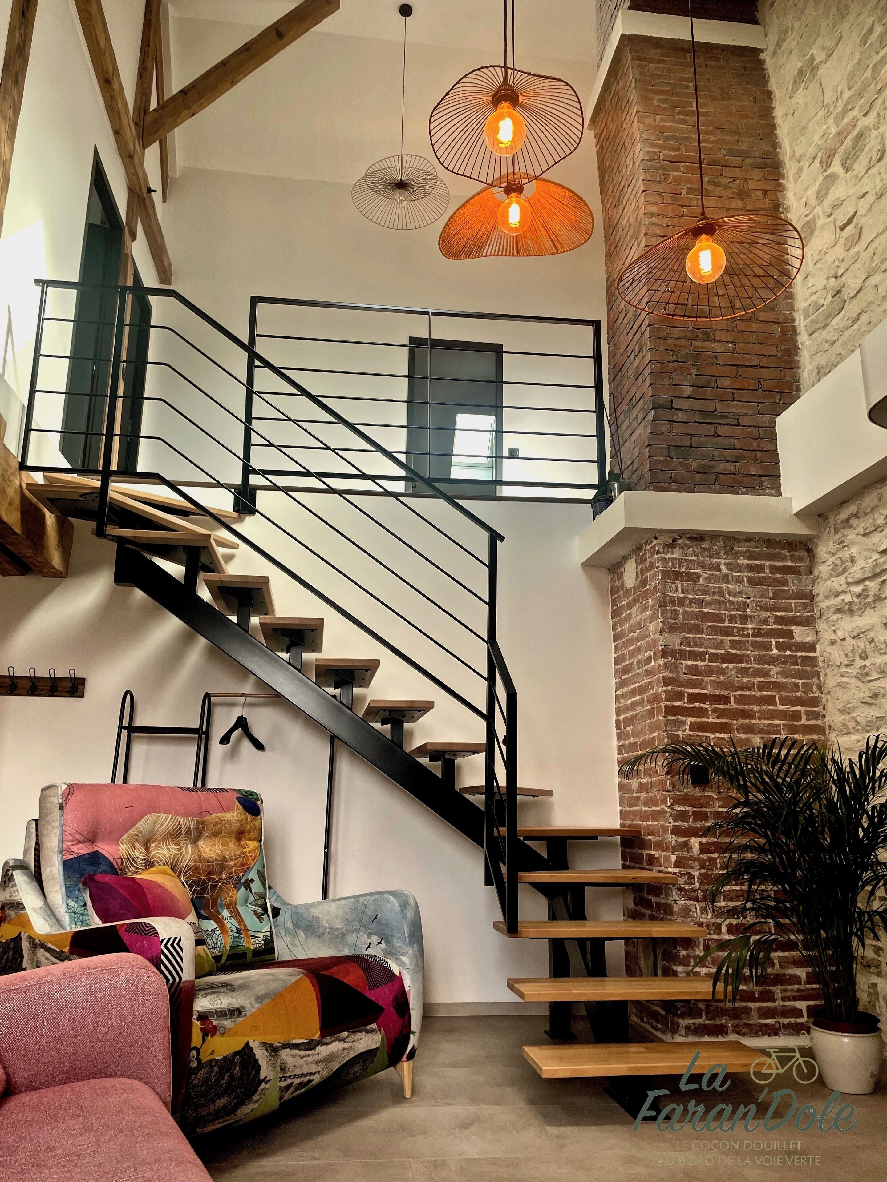 Un intérieur moderne avec un escalier, un canapé coloré et des lampes suspendues.