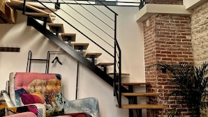 A modern interior with a staircase, a colorful sofa, and hanging pendant lights. - La Faran'dole - The cosy cocoon on the edge of the greenway. (Dole)