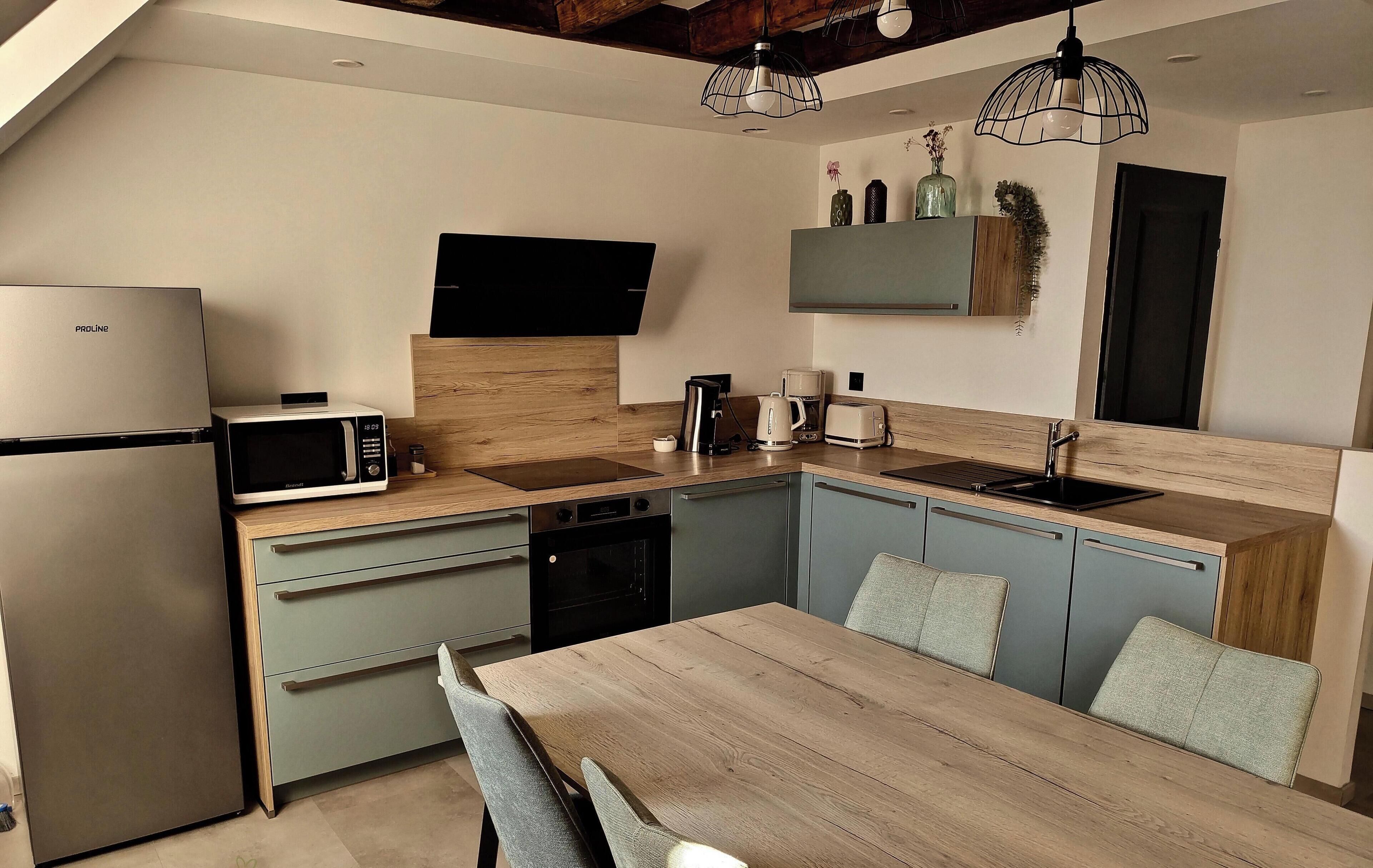 Cozinha moderna com micro-ondas embutido, cafeteira e máquina de lavar louça. Há uma mesa de jantar de madeira com cadeiras.