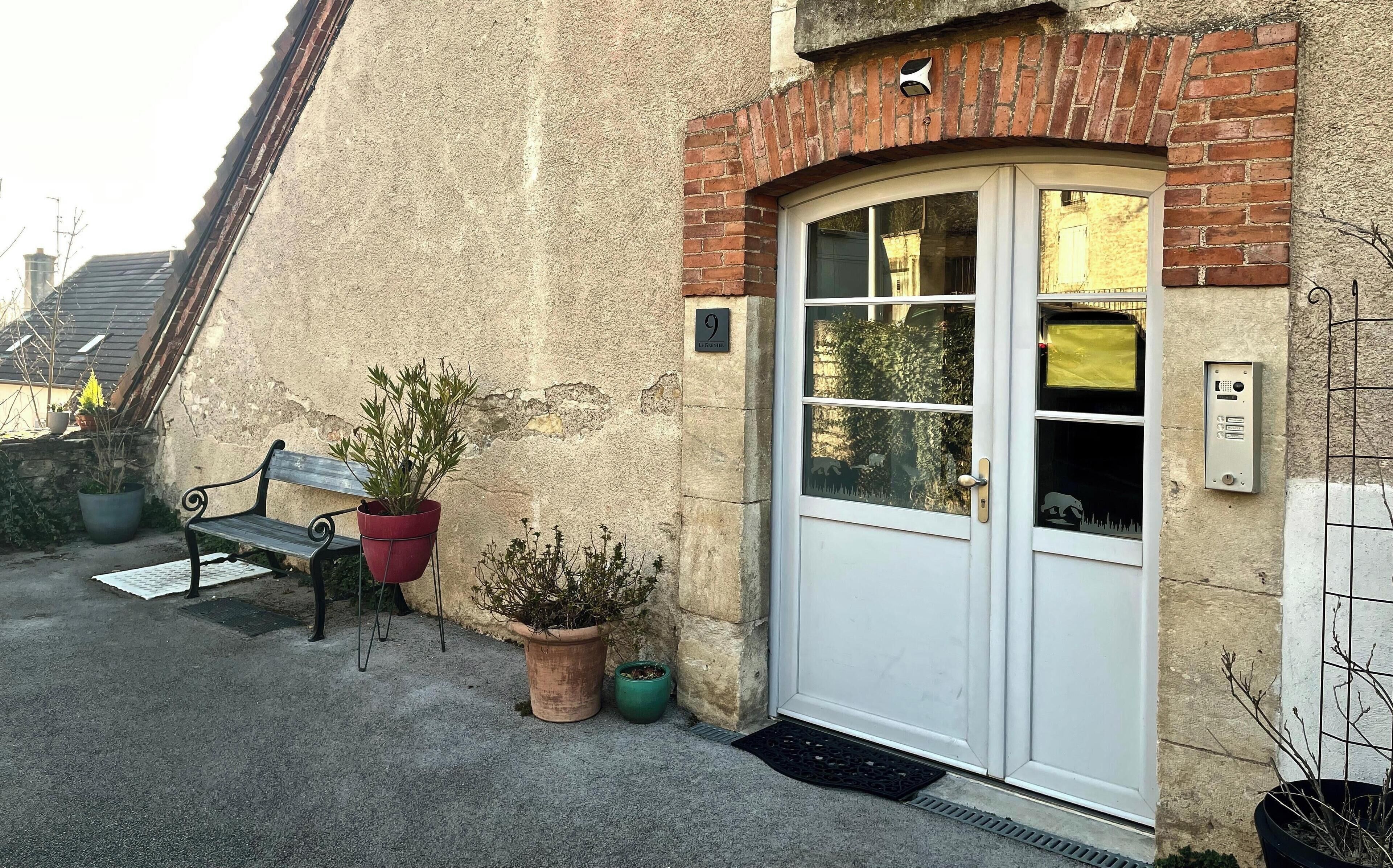 Un bâtiment avec une porte blanche, un banc et des plantes en pot.