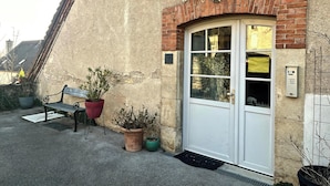 A building with a white door, a bench, and potted plants. - La Faran'dole - The cosy cocoon on the edge of the greenway. (Dole)