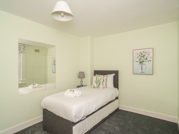 Une chambre à coucher avec un lit, une table de chevet, une lampe, un miroir et un tableau encadré accroché au mur.
