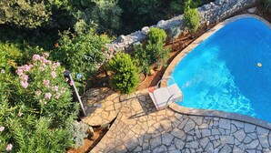A swimming pool with a stone deck and surrounding greenery. - Big Sea View apartment within walking distance of the old town, beach and shops (Krk)