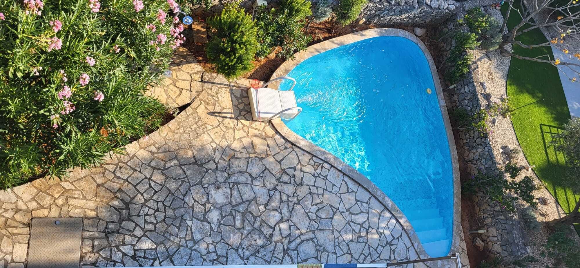 A swimming pool with a stone deck, surrounded by greenery and a stone wall.