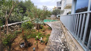 A stone pathway leading to a swimming pool, surrounded by various plants and trees. - Big Sea View apartment within walking distance of the old town, beach and shops (Krk)