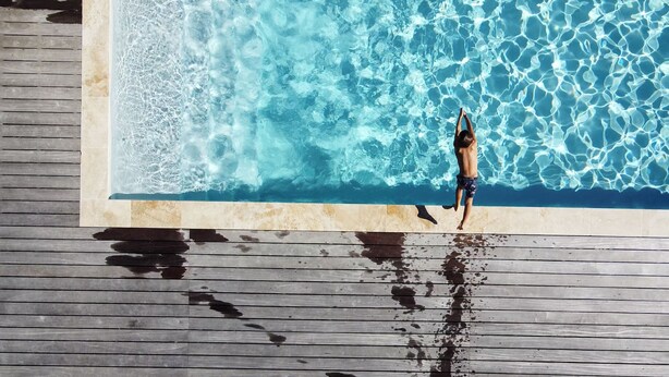 Eine Person springt von einer Holzterrasse in einen Swimmingpool.