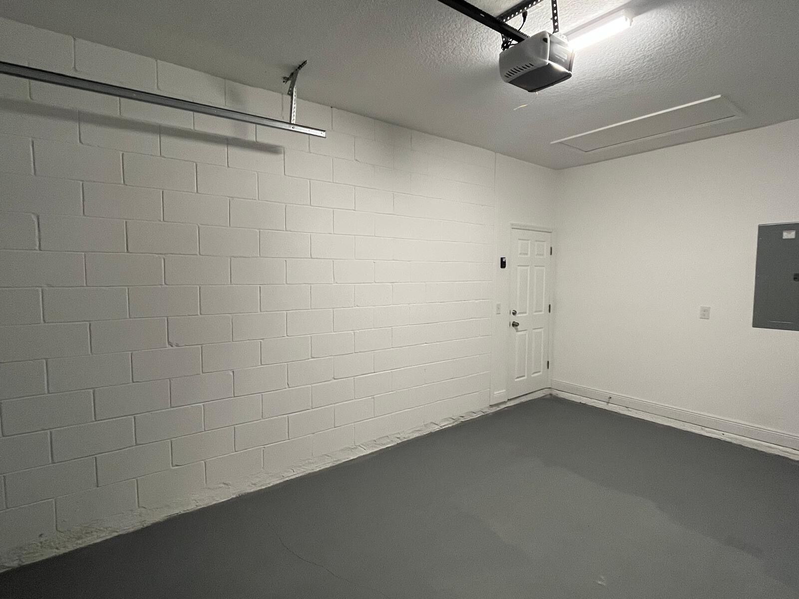 A clean, white-walled room with a door, a projector mounted on the ceiling, and a power outlet on the wall.