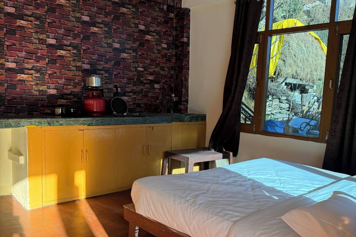 Ein Schlafzimmer mit Backsteinwand, einem Bett, einem Fenster mit Vorhängen und einer Küchenzeile mit Gasherd.