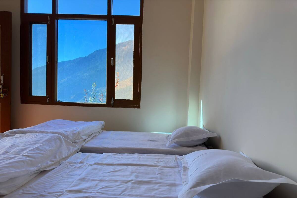 Ein Zimmer mit zwei Einzelbetten, einer Holztür und einem Fenster mit Blick auf die Berge.